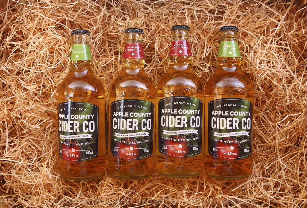 Bottles of Apple County Cider displayed against some hay.