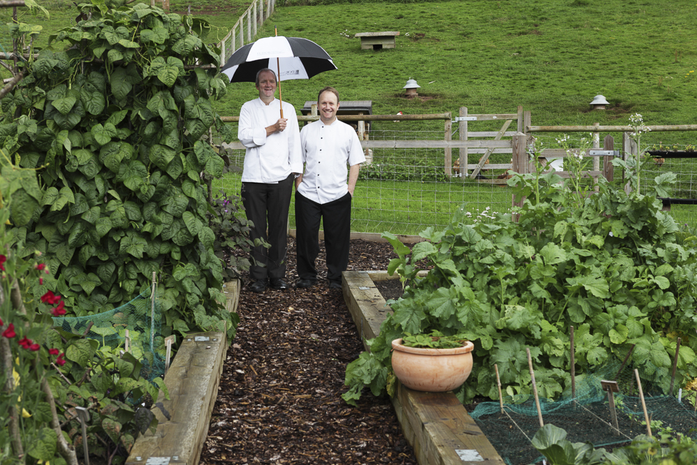 Two chefs in a garden sharing an umbrella